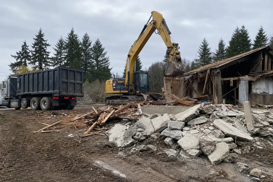 Excavator demolishing an old structure with a concrete and lumber debris pile in Vancouver, WA