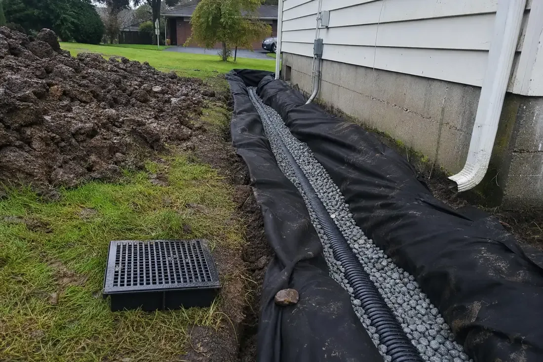 French drain trench with drain rock and perforated pipe along a house in Vancouver, WA